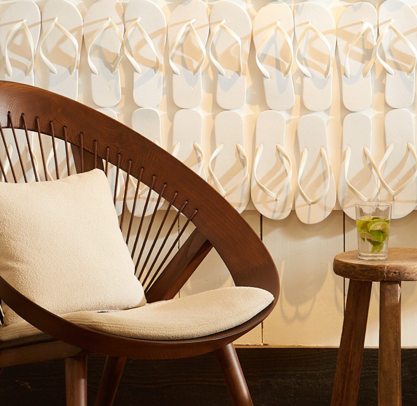 A wooden armchair with cream cushion in front of a wall of white flip-flop decorations at Down Under