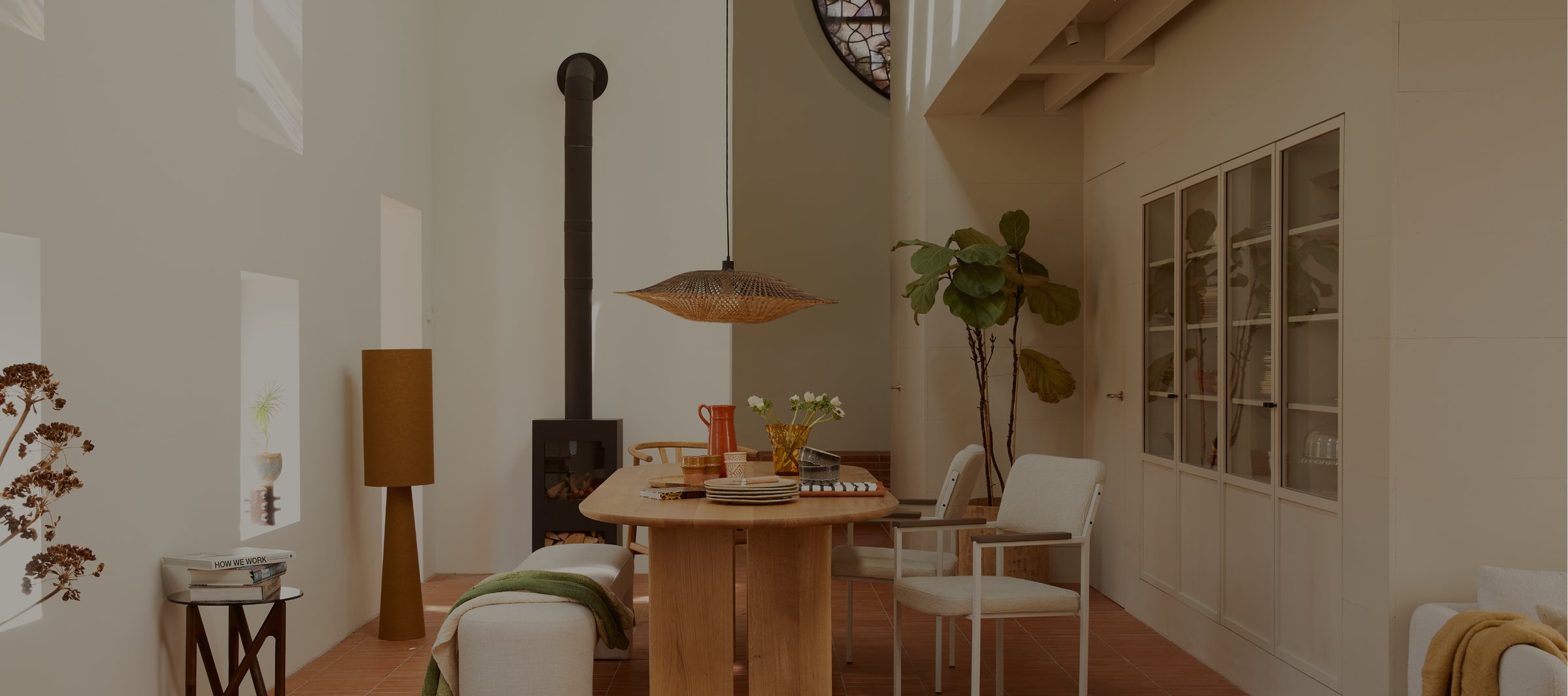 Styled dining area in the Het Kabinet Wonen showroom, with a wood-burning stove and a rattan pendant lamp