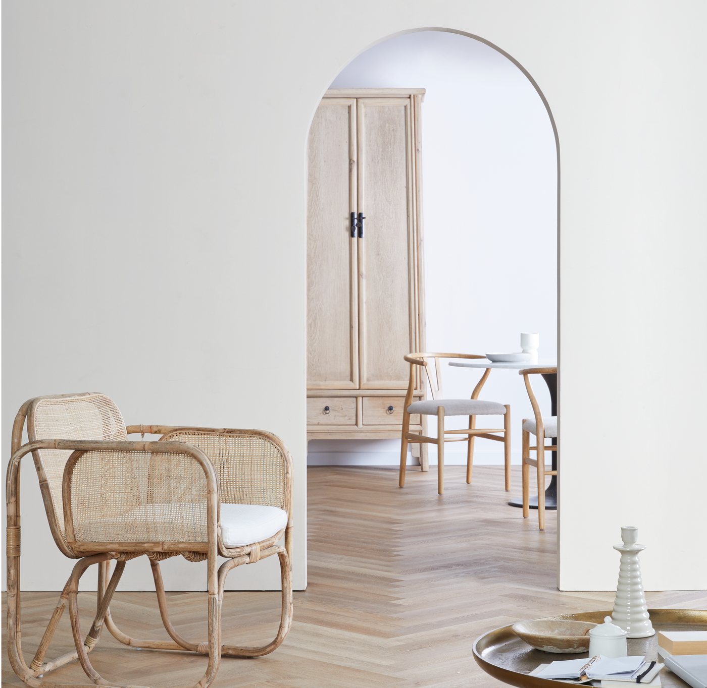 A rattan chair in the foreground, with an arched doorway opening onto a cabinet and dining set