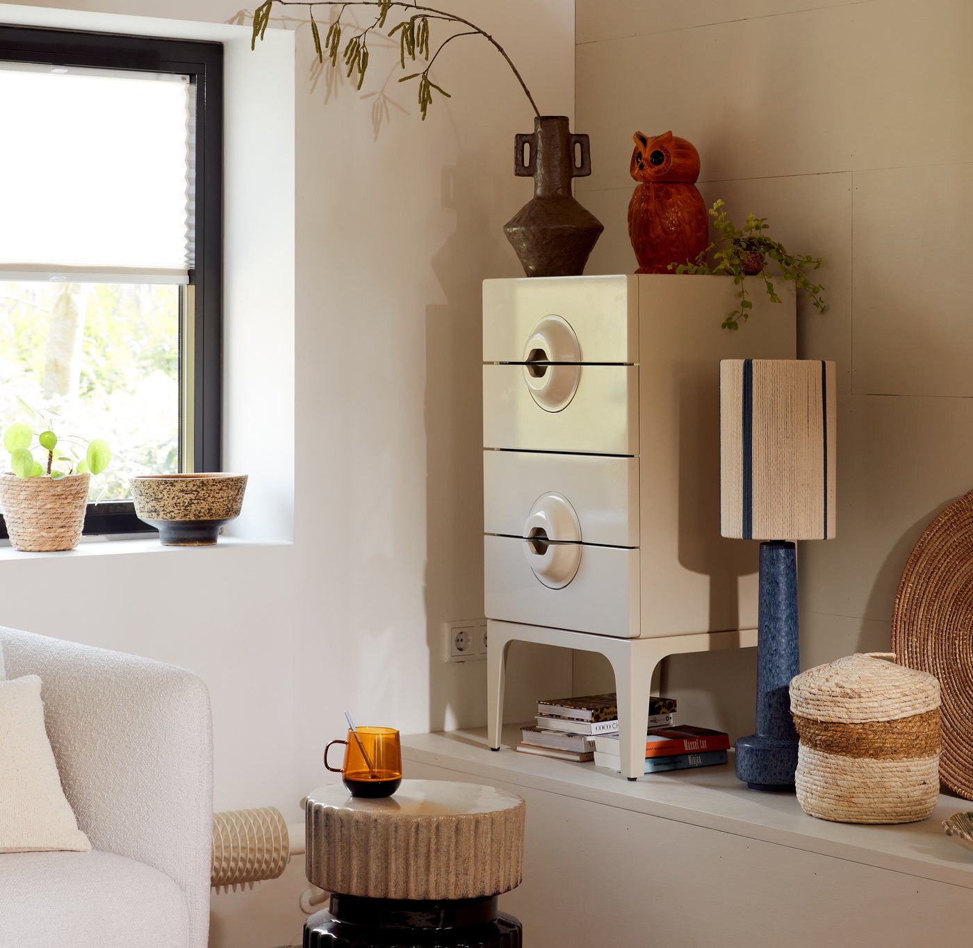 A styled cabinet vignette with a ceramic owl, vase and table lamp