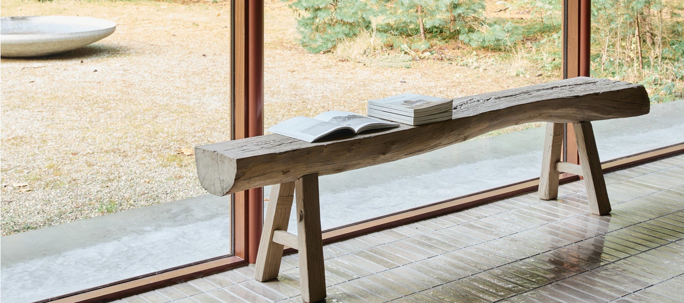 A weathered oak bench styled with vintage books, forest view behind
