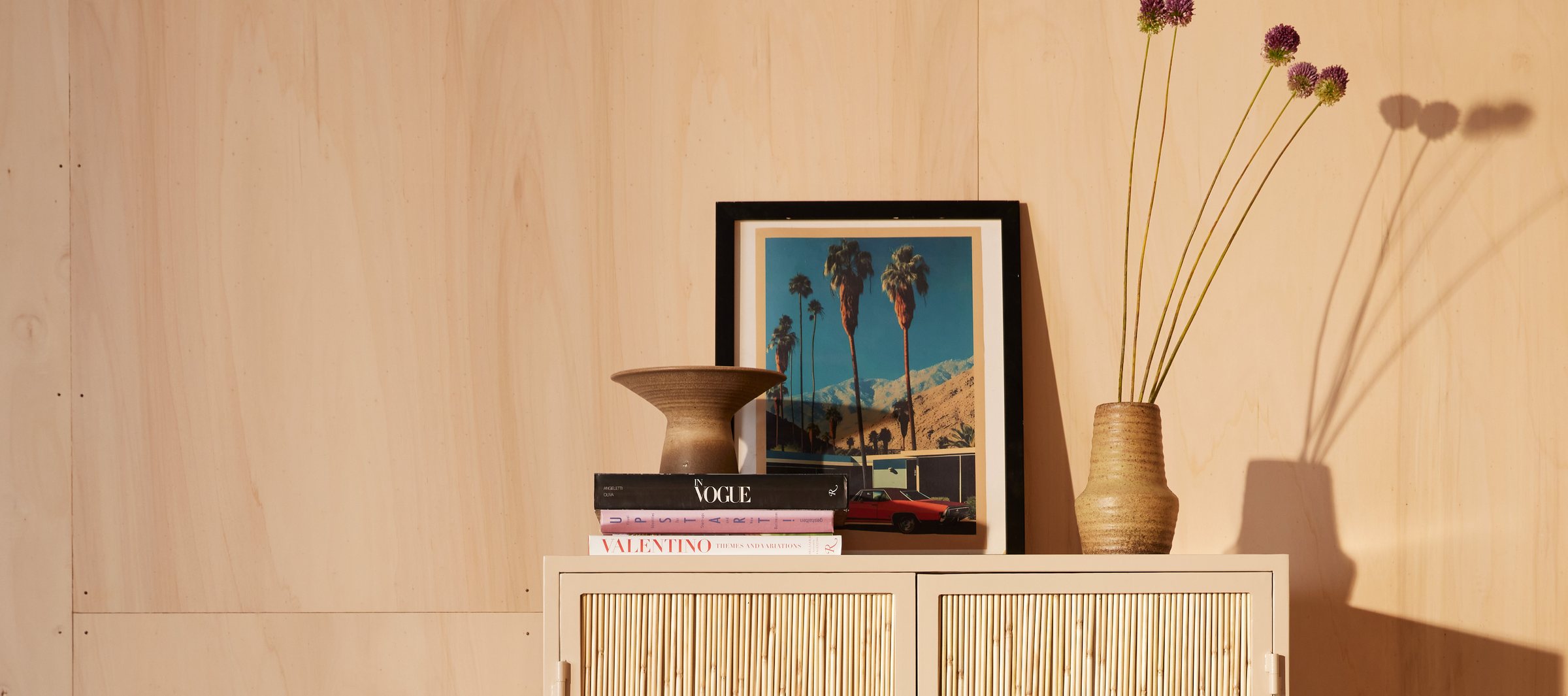 A cream New Routz cabinet with rattan doors, styled with ceramics, books and a framed print