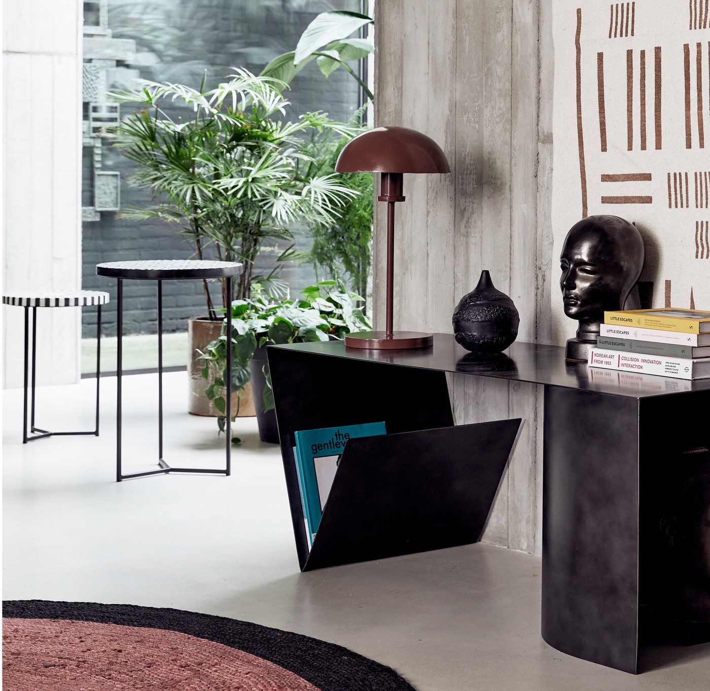A black New Routz console table styled with ceramics and books in a plant-filled interior